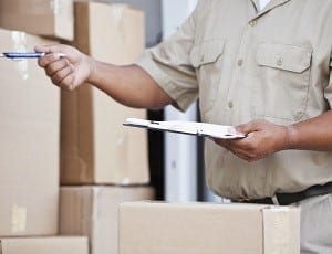 Man delivering packages, asking for customer signature. Focus on hand holding clipboard.